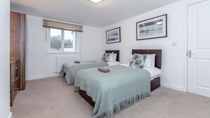 A bedroom with two beds, a window with blinds, a radiator, and framed pictures on the wall. - Royal Apartments RA2 (Greater London)