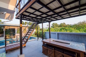 Un espacio al aire libre cubierto con piscina, terraza de madera y una mesa con bancos.