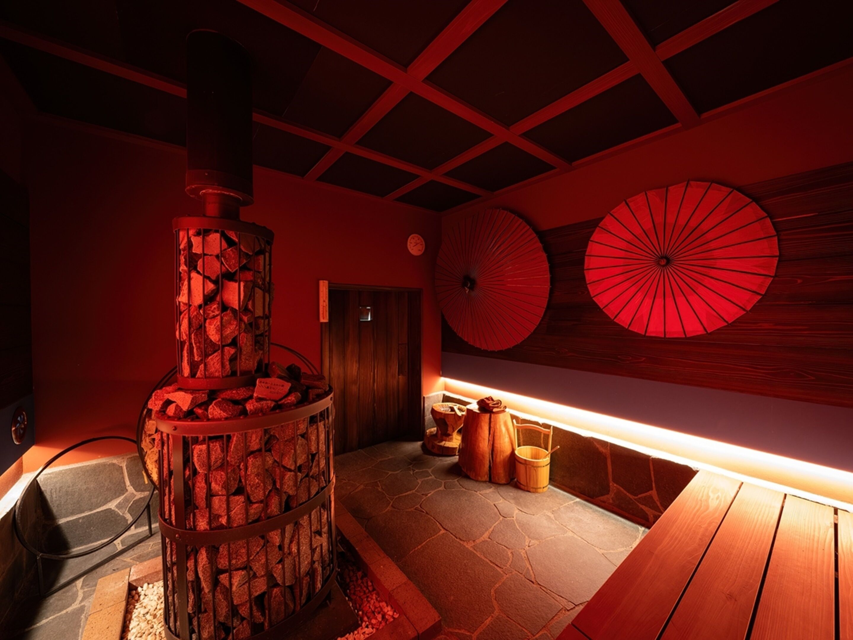 A sauna room with a stone floor, a wooden bench, and a stone pillar with a firebox.