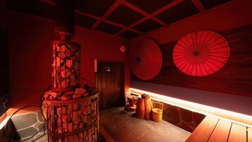 A sauna room with a stone floor, a wooden bench, and a stone pillar with a firebox.