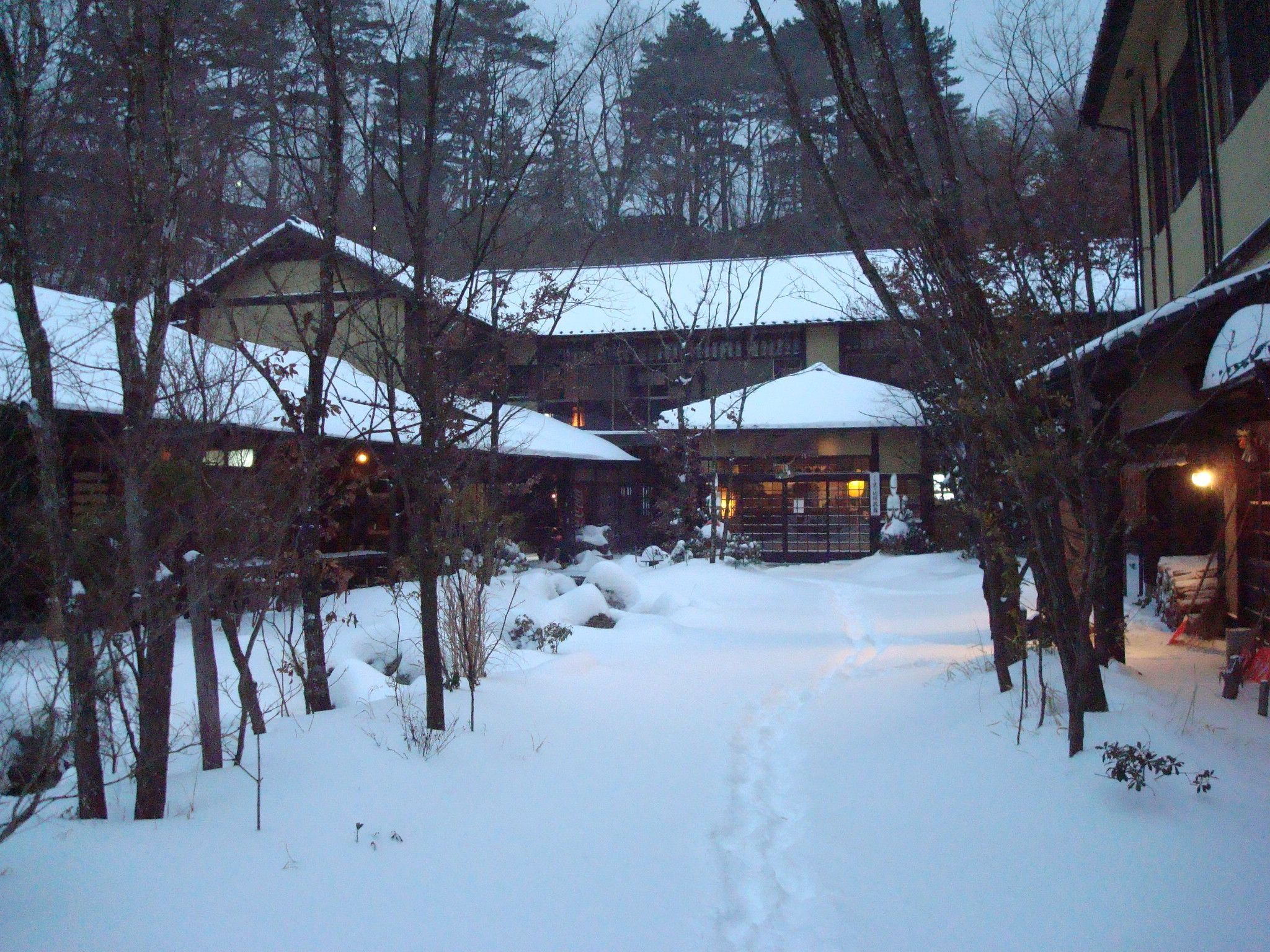 A snow-covered courtyard with buildings, trees, and a visible path.