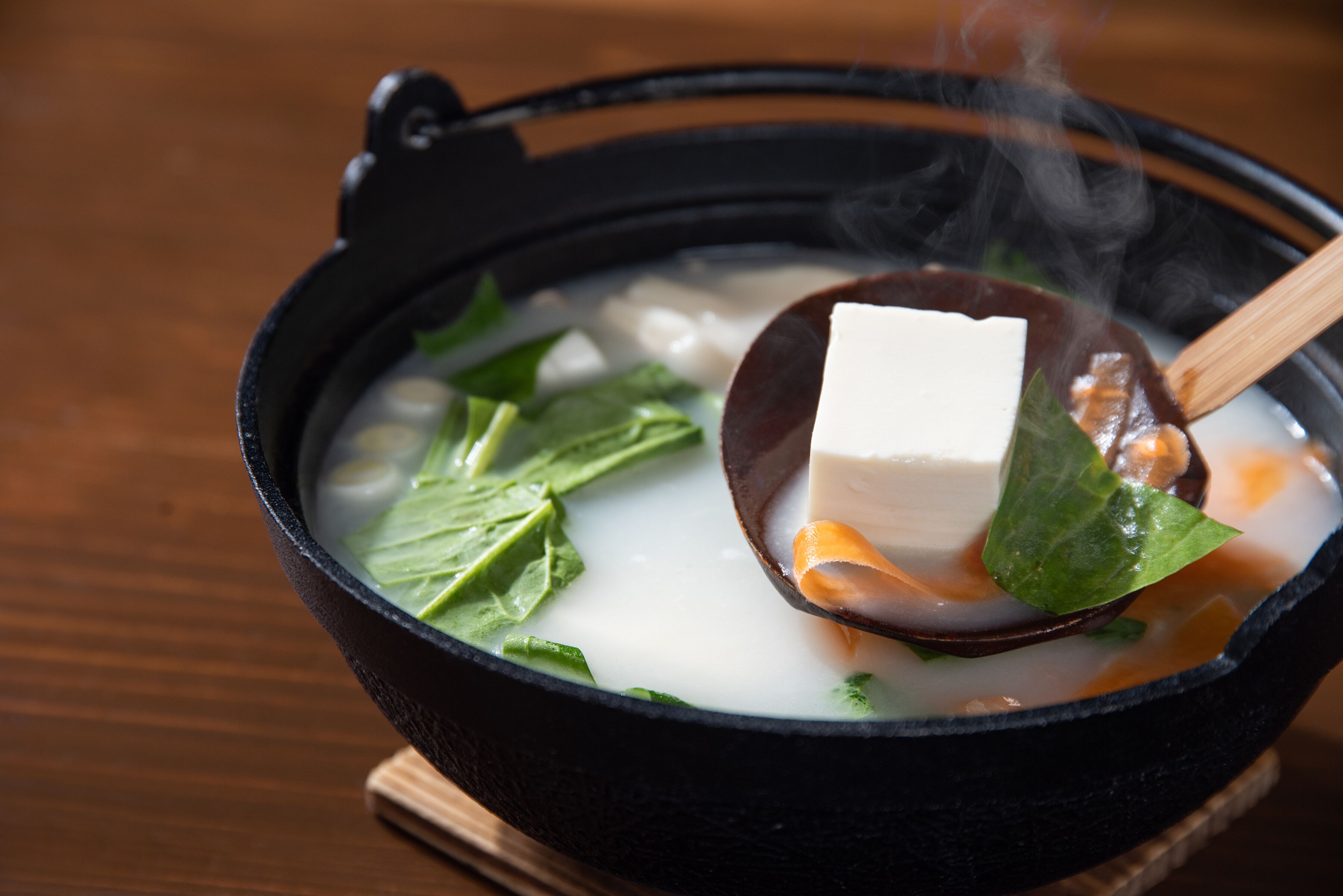 Un tazón de sopa con tofu y hojas verdes, vapor saliendo del tazón.