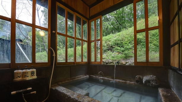 Ein Thermalbad mit Steinwänden und Holzfenstern, umgeben von üppiger Vegetation.
