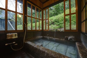 A hot spring bath with stone walls and wooden windows, surrounded by lush greenery. - Kanno Jigoku (Kokonoe)
