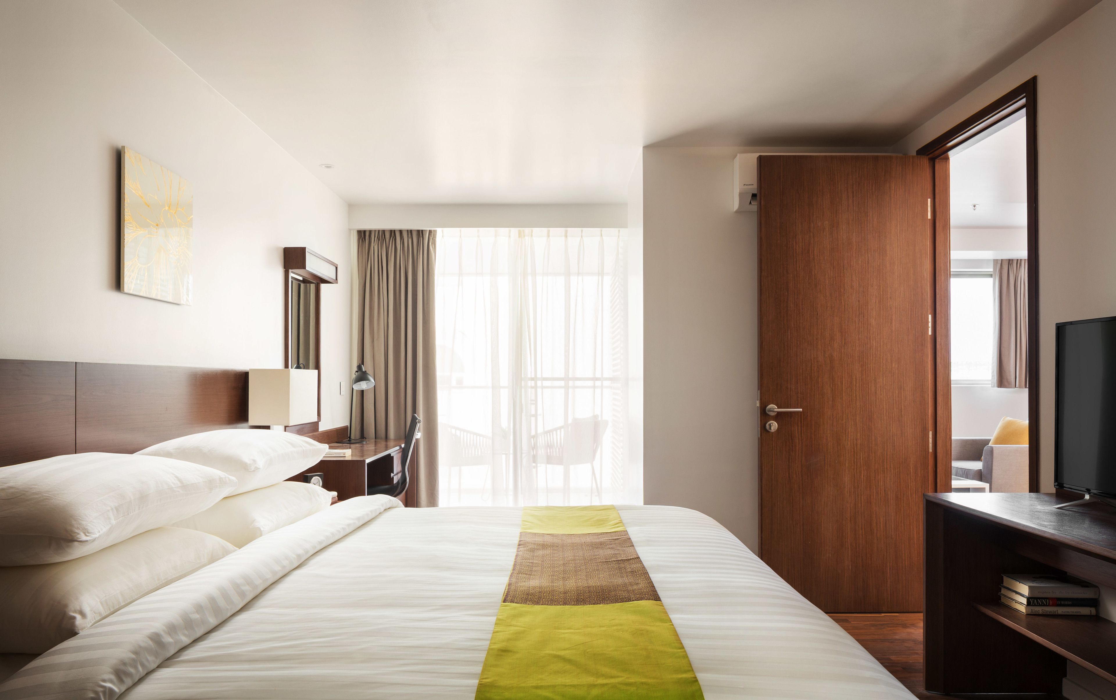 A hotel room with a bed, a desk, a chair, a TV, and a door.