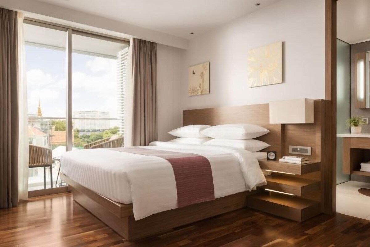 A modern hotel room with a large bed, a nightstand, a mirror, and a view of the city.