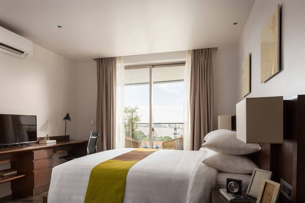 A hotel room with a bed, desk, TV, and a view of the outdoors.