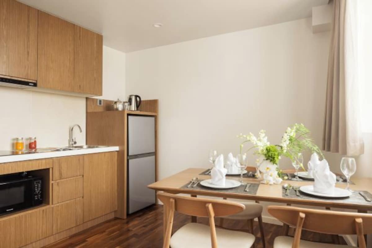 Una cocina moderna con armarios de madera, horno empotrado y una zona de comedor preparada para cuatro personas, con vajilla blanca.