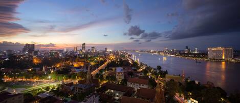 A cityscape at dusk with a river, illuminated buildings, and traditional architecture.