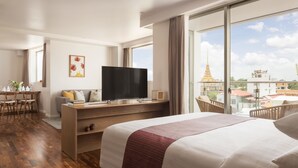 A hotel room with a large bed, a desk with a TV, a balcony with a view of a temple and buildings. - Hotel Emion Phnom Penh (Phnom Penh)