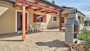 A covered patio with a stone fireplace, white chairs, and a table. - Holiday apartment with air conditioning and Internet (Savudrija)
