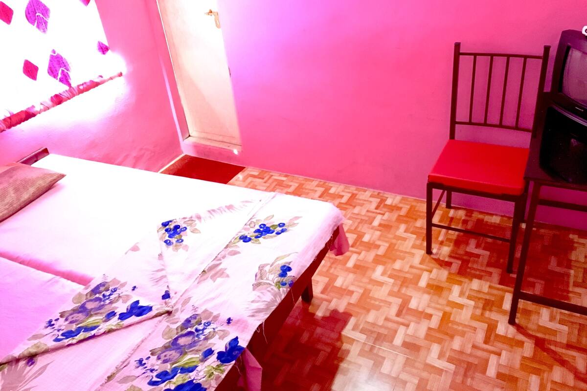 A room with a bed, a chair, a television, and a door.