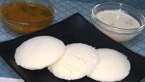 Drei weiße runde Objekte auf einer schwarzen Platte, begleitet von zwei kleinen Saucenschalen.