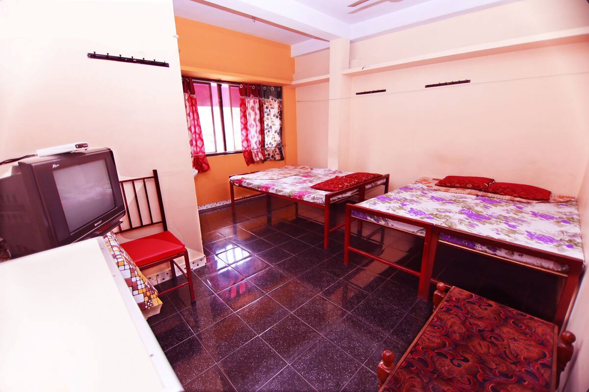 A compact room with a bed, a small table, a television, and a window with curtains.