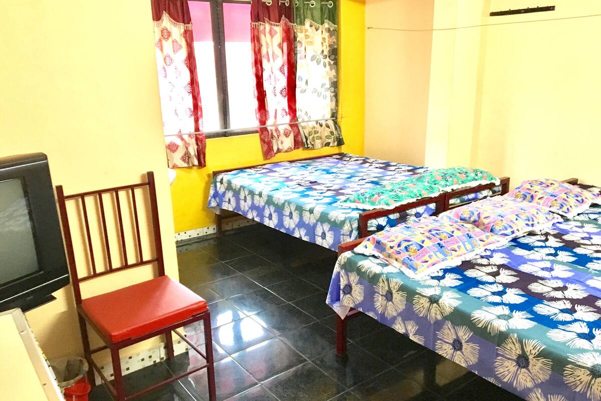 A room with two beds, a chair, a television, and a window with curtains.