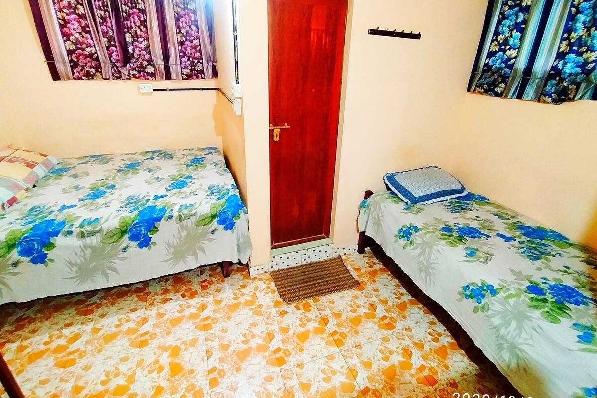 A small, two-bed room with floral-patterned bedding, a wooden door, and a tiled floor.