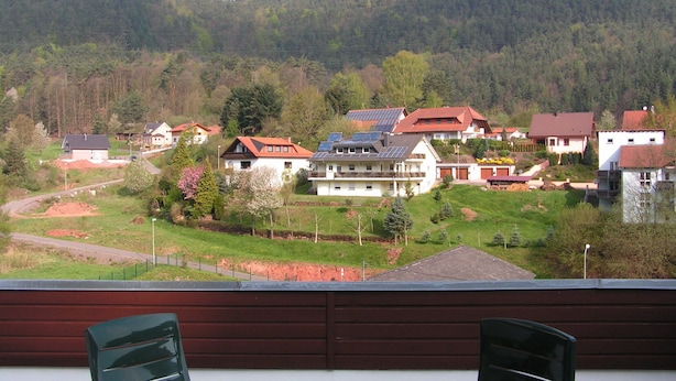 Ein Wohngebiet mit Häusern, einige davon mit Solaranlagen, umgeben von Grünflächen und Hügeln.