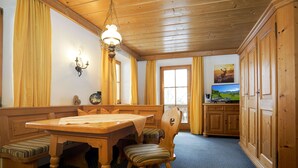 Uma mesa de jantar de madeira com cadeiras, um candelabro e uma televisão em um quarto com armários de madeira e carpete estampado.