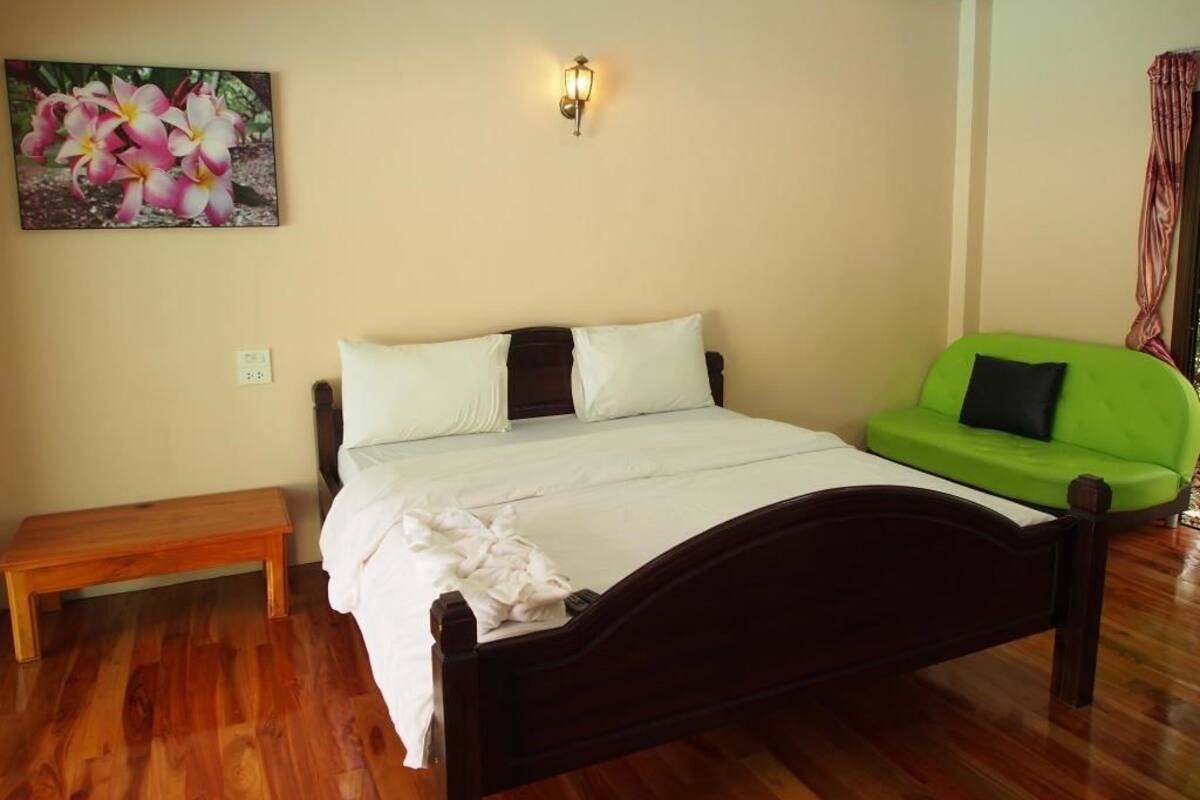 Un dormitorio con cama de madera, un banco, un sofá verde y un aplique de pared.