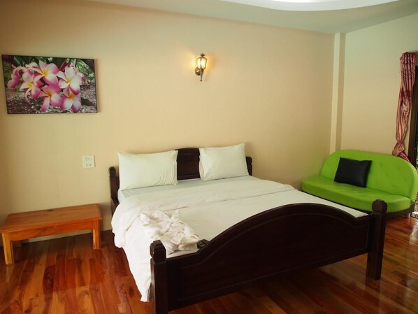 A bedroom with a wooden bed, a bench, a green sofa, and a wall-mounted light fixture.