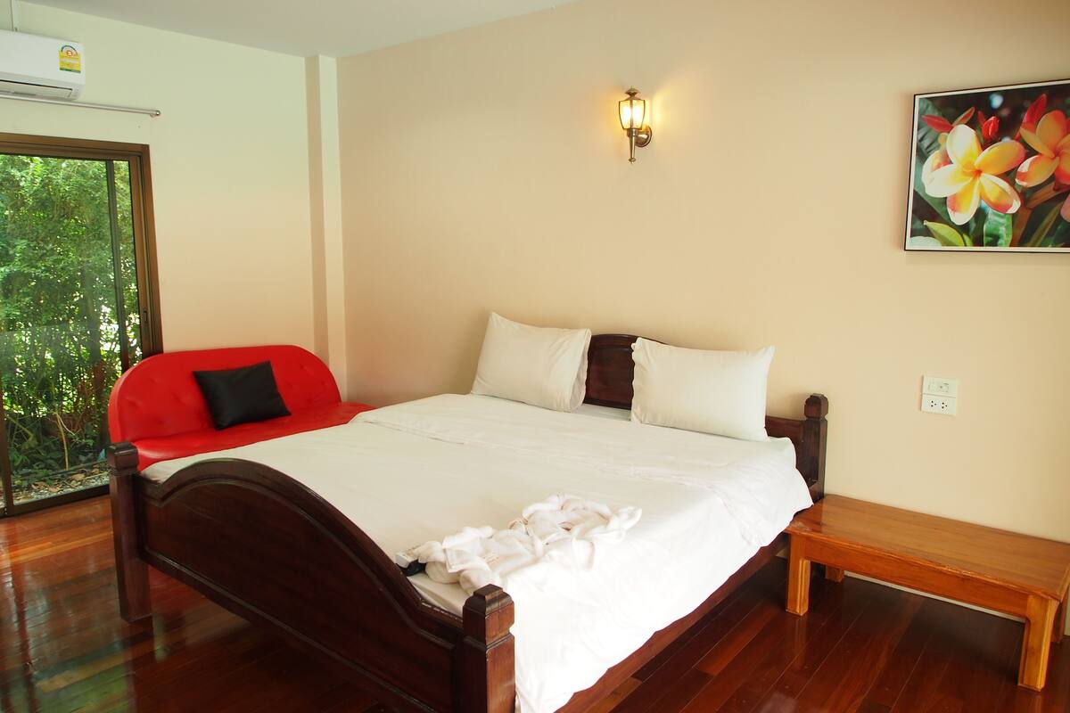 Un dormitorio con una cama de madera, un sofá rojo, un banco y un cuadro de flores.