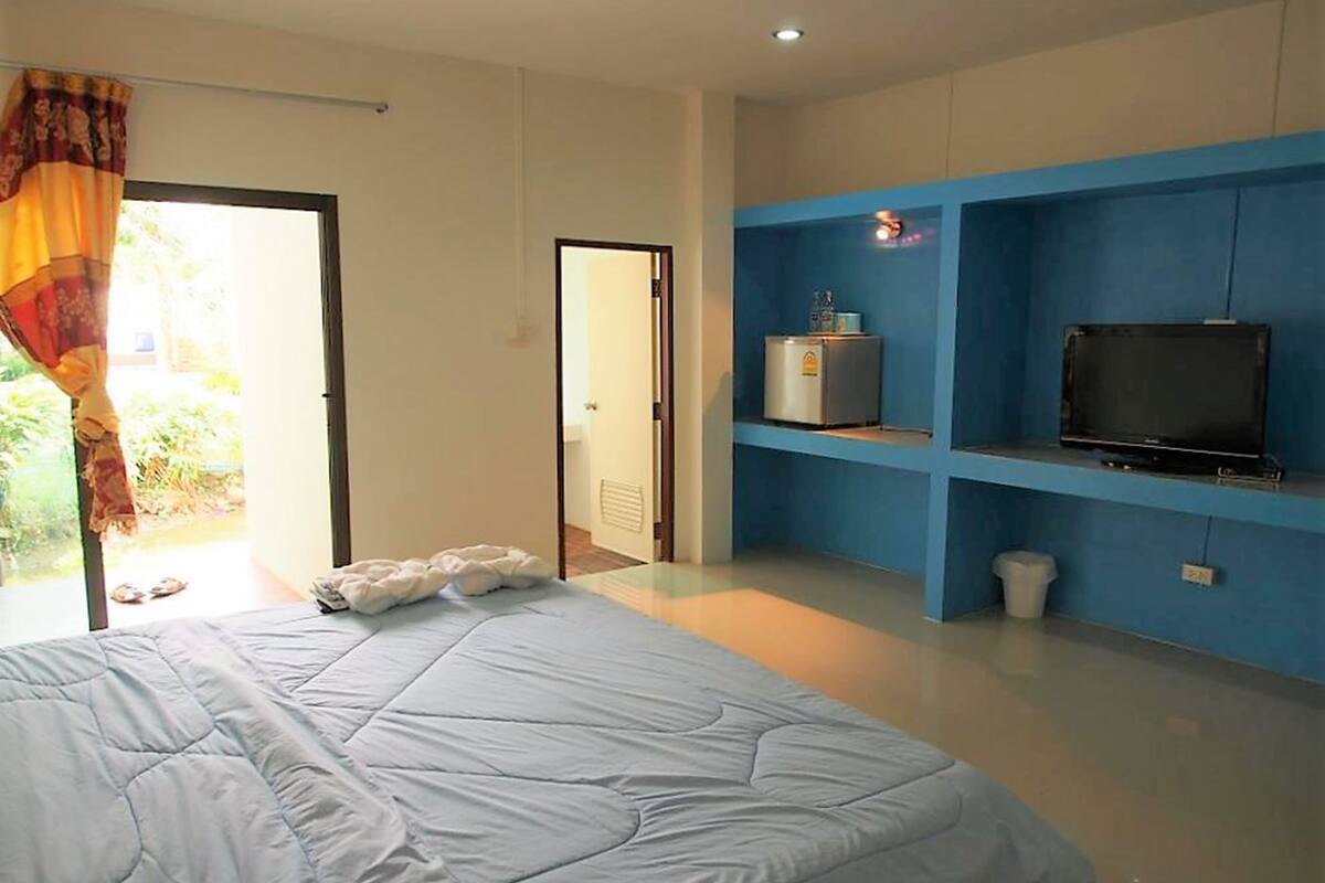 Un dormitorio con una cama, un televisor sobre un estante azul y un refrigerador.