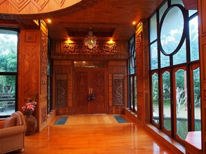 A wooden interior with large windows, a chandelier, and a door with intricate carvings.