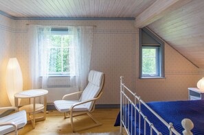Una habitación con una cama, un sillón mecedora, una mesita y una ventana.