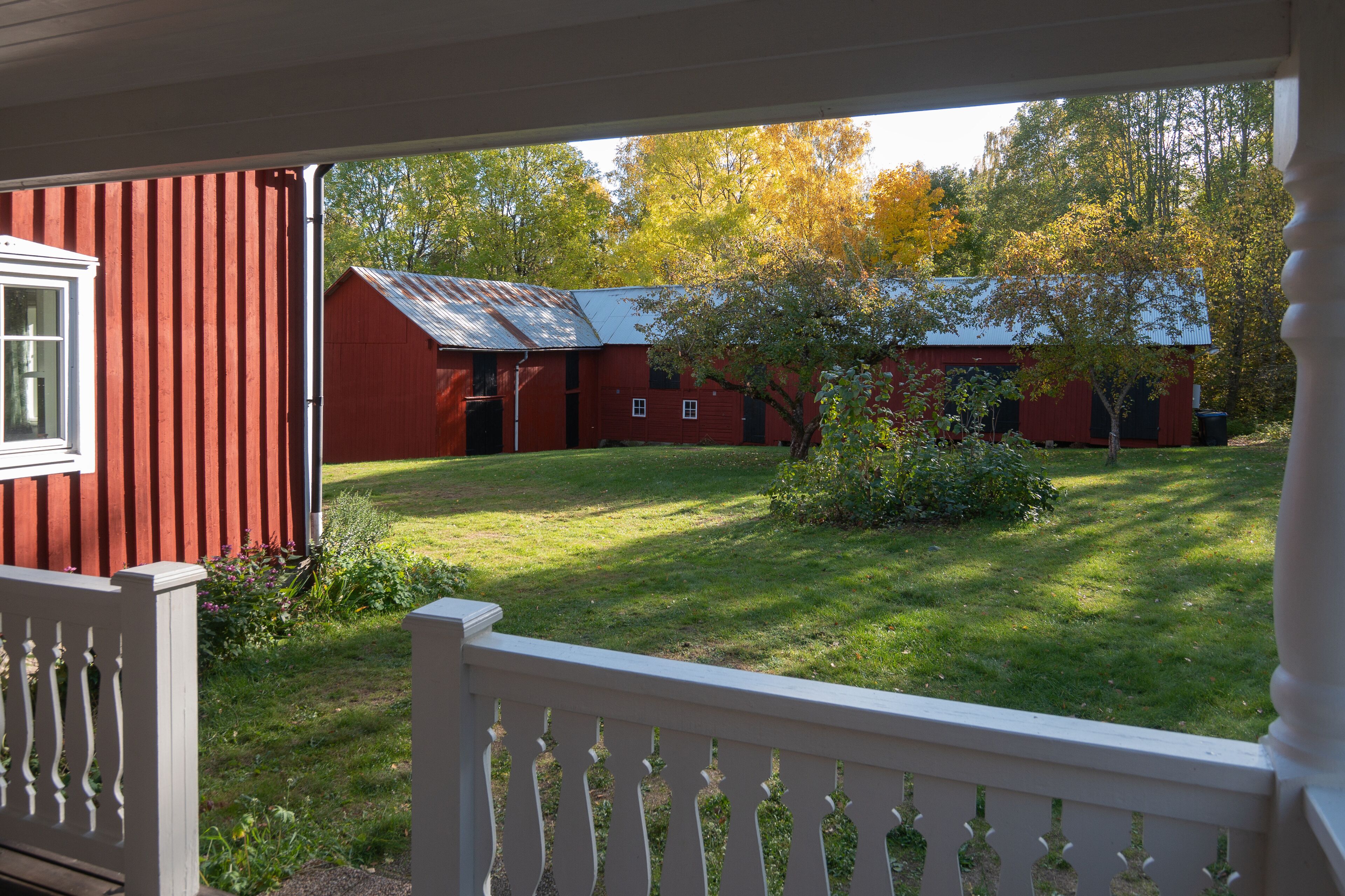 Ein rotes Bauernhaus mit weißem Veranda und einem gepflegten Rasen.