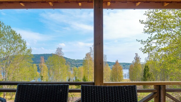 A wooden deck with wicker chairs and a table, overlooking a lake and forested hills.