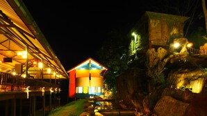 A building with a red and blue facade, a covered outdoor area with tables, and a natural landscape with rocks and a small pond. - Aiyara Garden Resort (Chanthaburi)