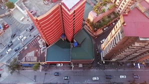 Vue aérienne d’un hôtel à la façade distinctive, aux couleurs rouge et marron, doté d’une piscine sur le toit et d’un espace de stationnement.