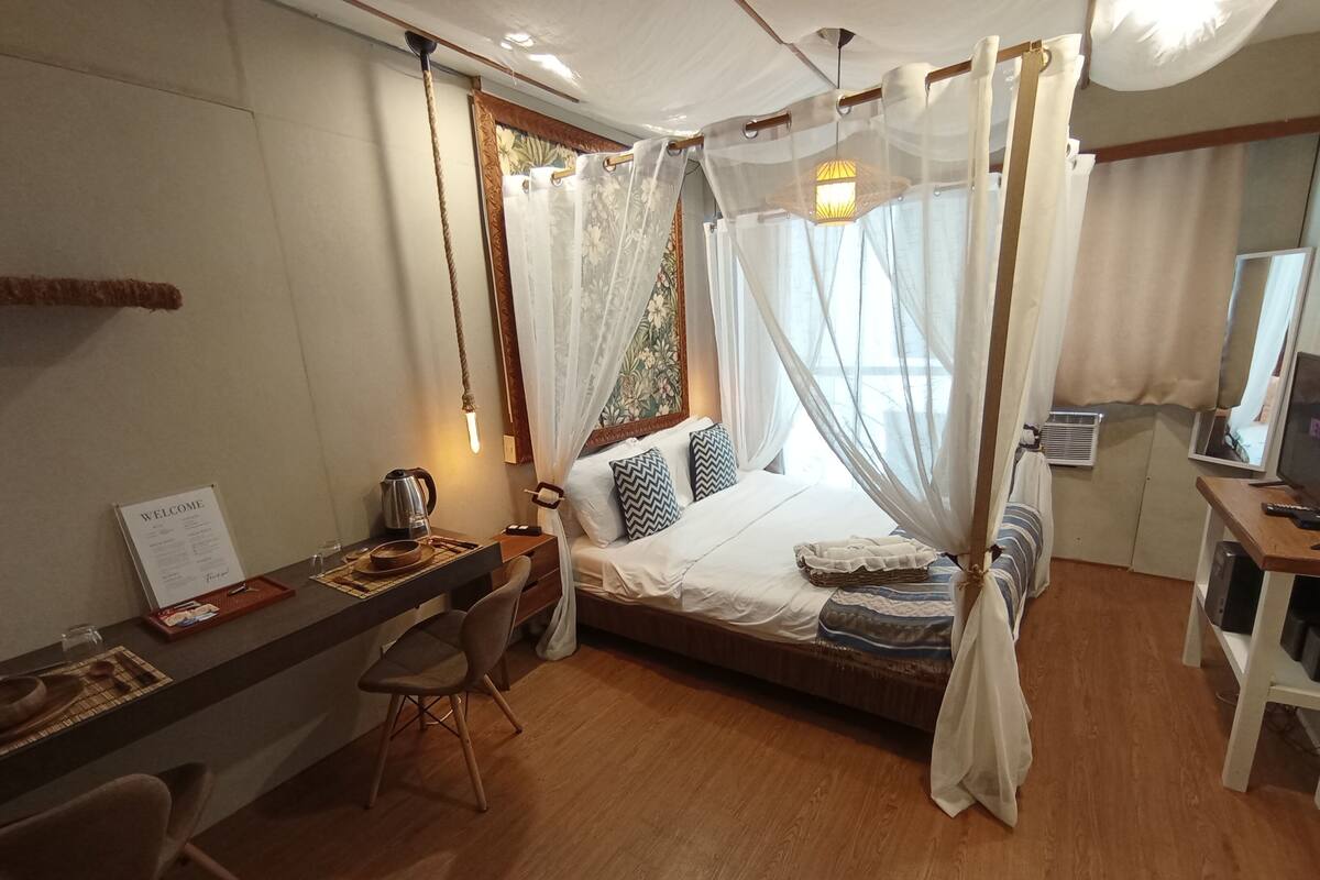 A room with a bed, a desk, a chair, a bedside table, a lamp, a television, and a window with curtains.