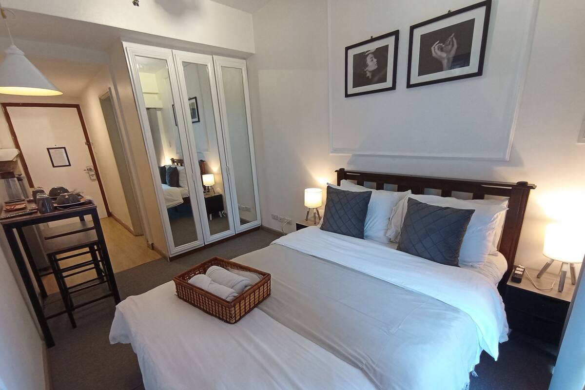A hotel room with a bed, a desk, a wardrobe, and two framed pictures on the wall.