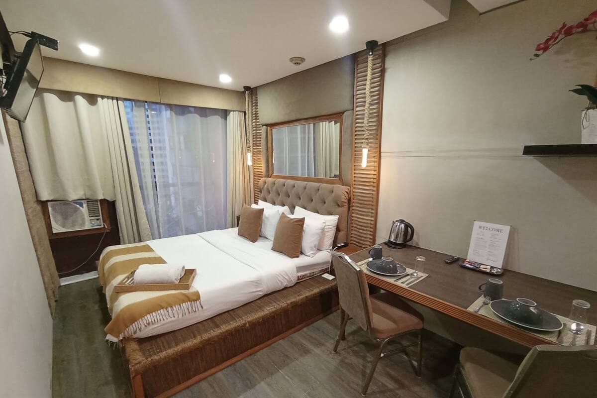 A hotel room with a large bed, a desk with a chair, a coffee maker, and a welcome sign.