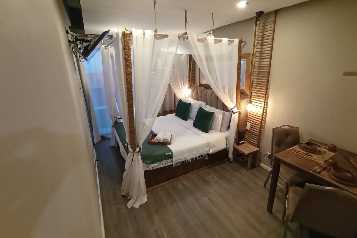 A bedroom with a bed, bedside table, chair, and a small table with a tray.