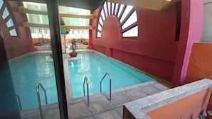 Une piscine intérieure à l’eau claire, entourée de murs rouges et dotée d’un sol carrelé.