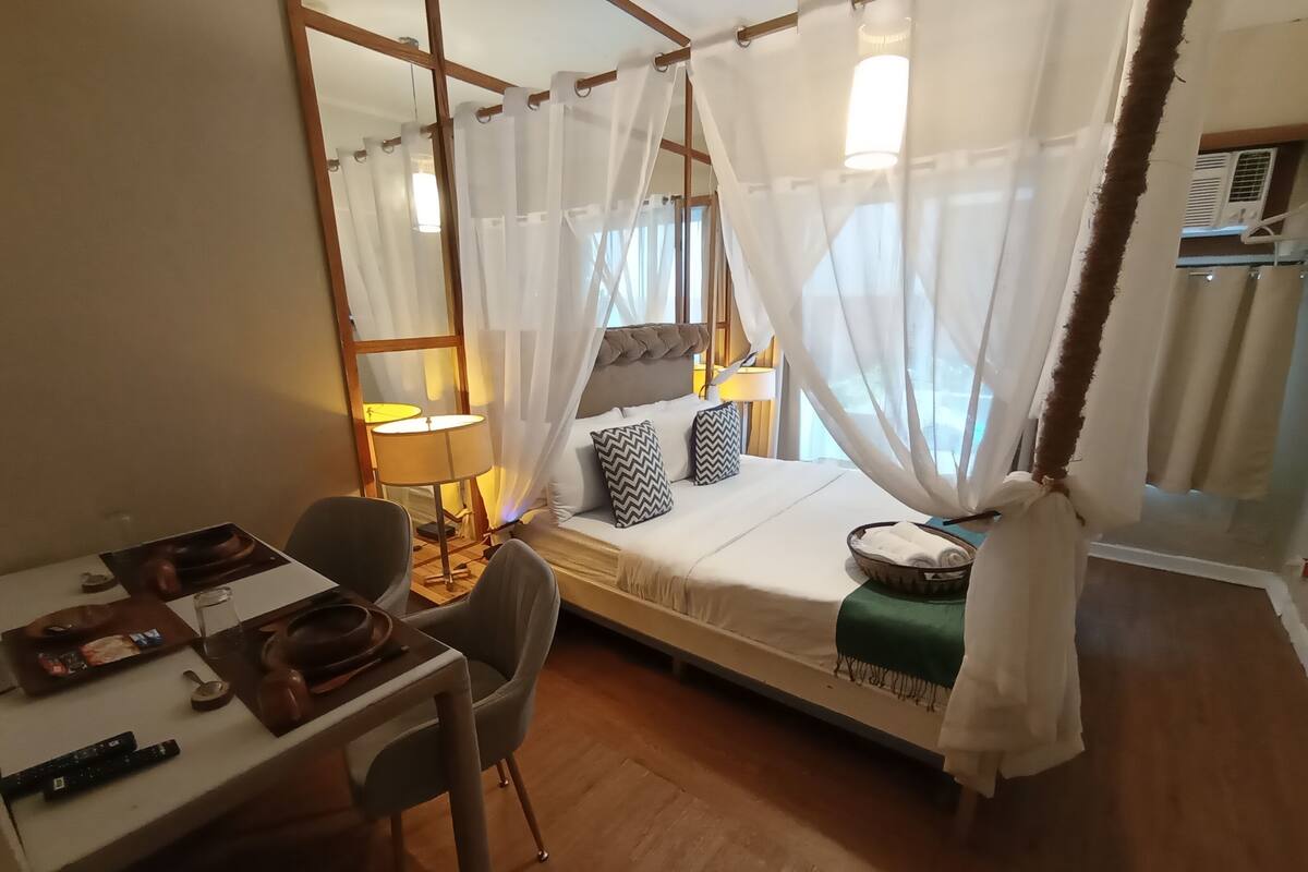 A bedroom with a bed, a desk, a chair, a lamp, and a window with curtains.