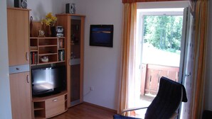 Una sala de estar con televisión, armarios de madera, un sillón y vistas a través de una puerta.