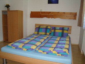 A bedroom with a bed, a wooden wardrobe, and a wooden headboard.