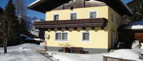 Um edifício de dois andares com varanda, rodeado por neve e montanhas.