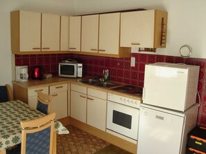 Een kleine keuken met eenvoudige apparatuur, een zithoek met een tafel en stoelen, en een vloer met een patroon.