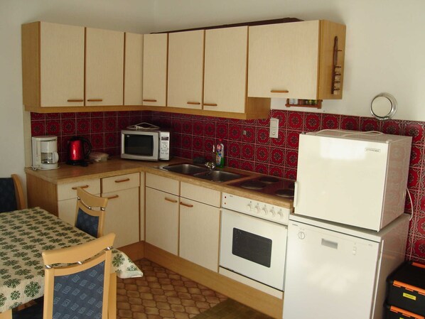 A compact kitchen with basic appliances, a dining area with a table and chairs, and a patterned floor.