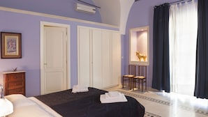 A bedroom with a bed, two chairs, a desk, a mirror, and a window with curtains. - Villa Urso BedWine (Lecce)