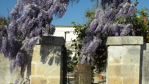 A stone archway with purple flowers, leading to a building with a white facade. - Villa Urso BedWine (Lecce)
