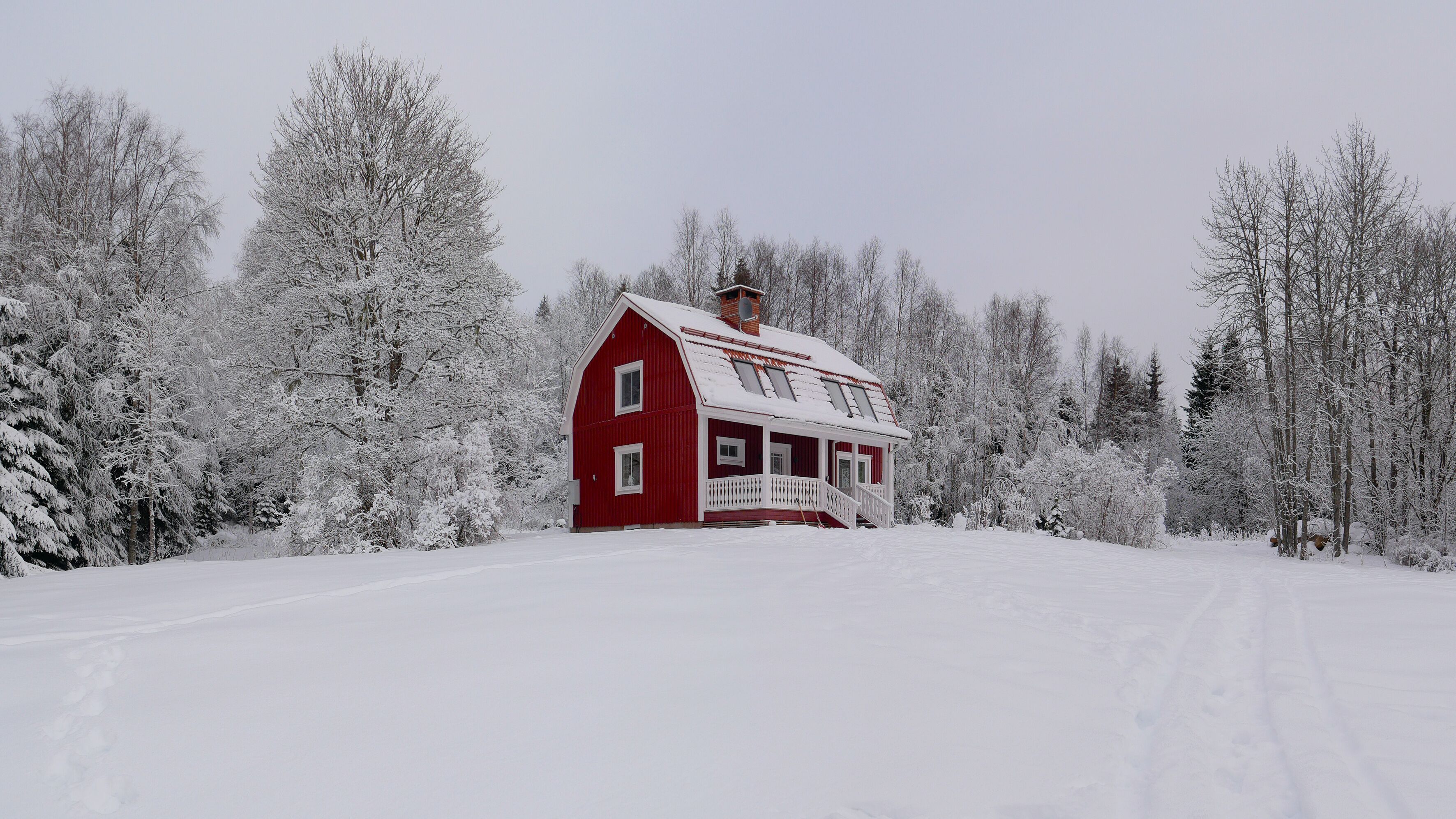 A red barn with a white porch and a chimney, surrounded by snow-covered trees.