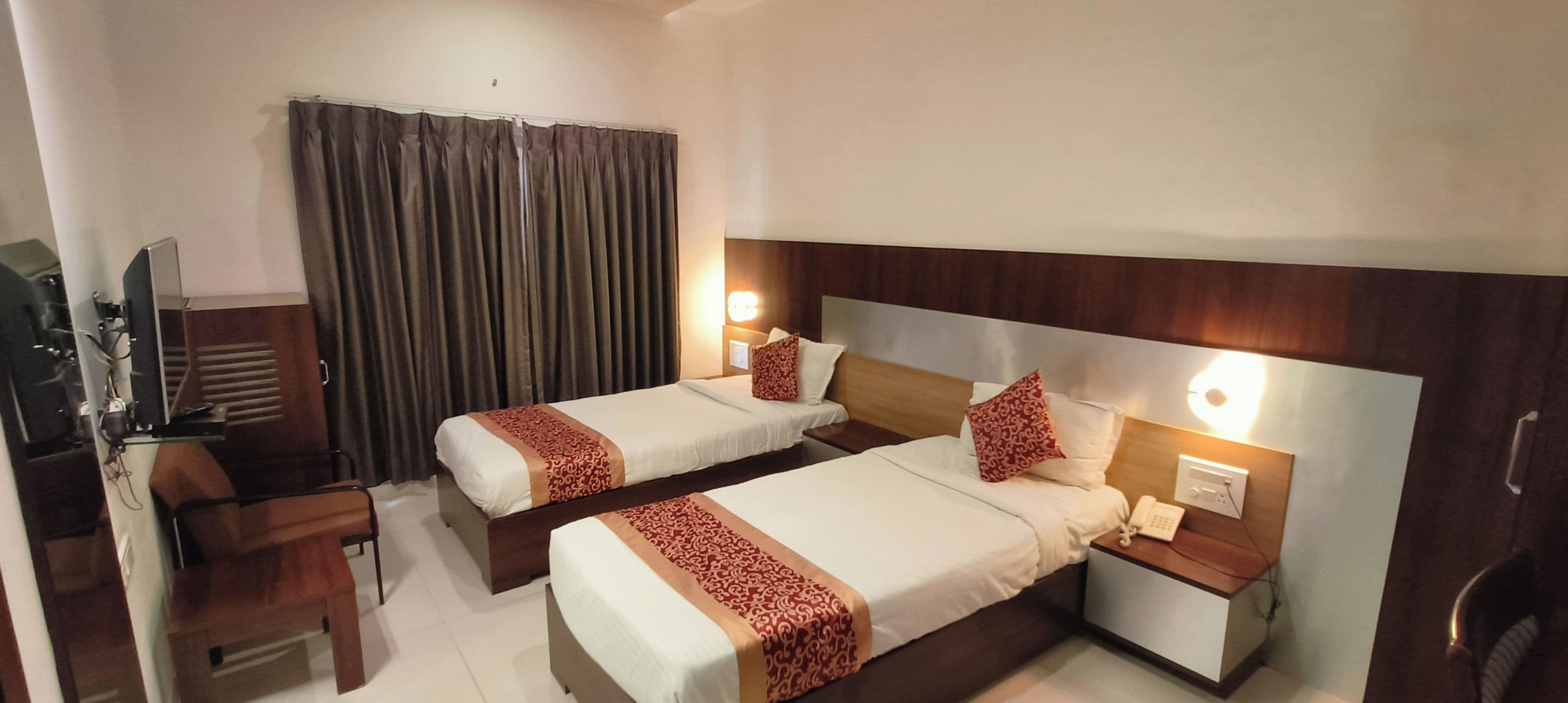 A hotel room with two beds, a desk, a chair, a television, and a curtain.