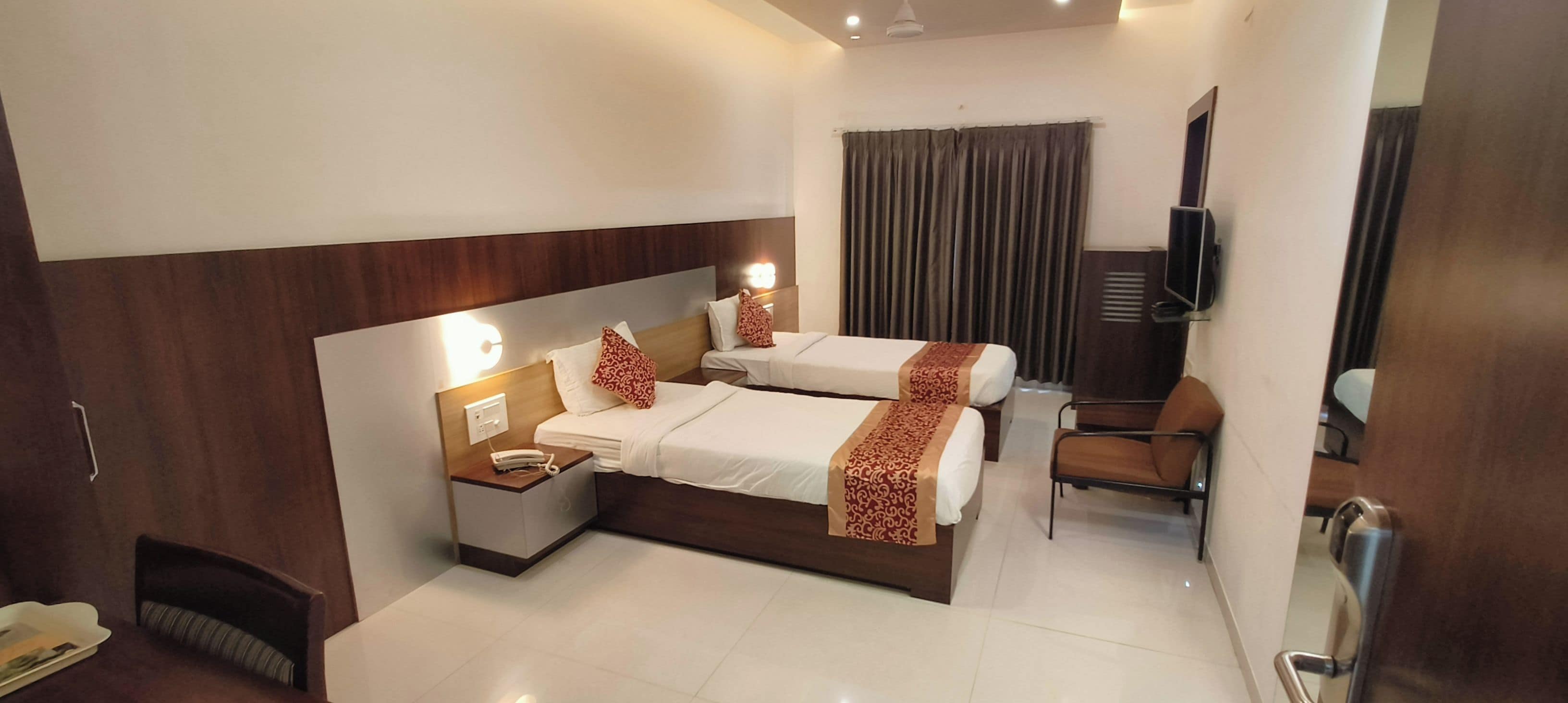 A hotel room with two beds, a desk, a chair, a TV, and a mirror.