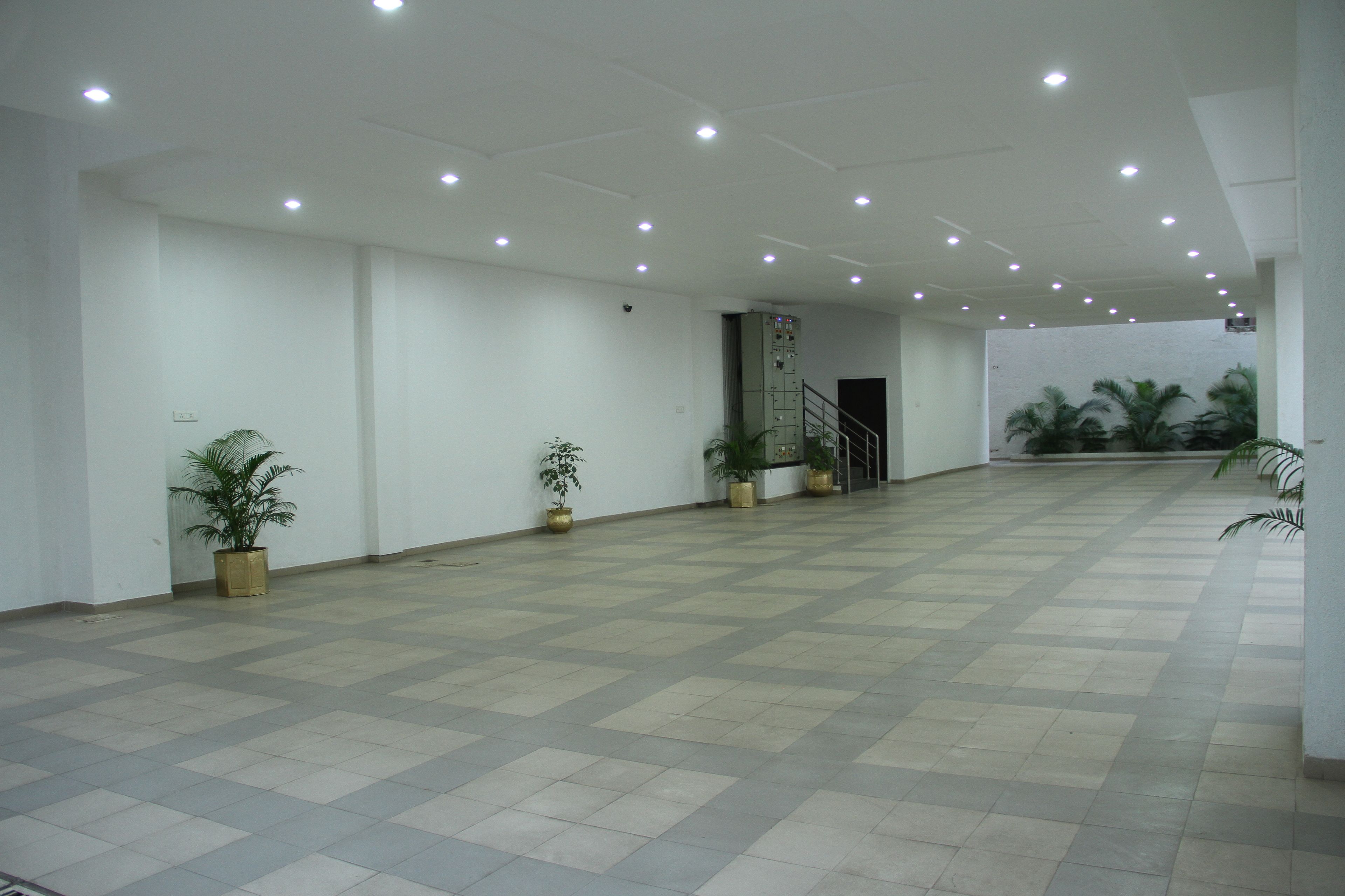 A spacious indoor area with a tiled floor, white walls, and several potted plants.