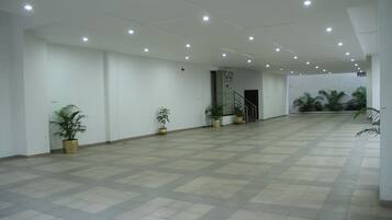 A spacious indoor area with a tiled floor, white walls, and several potted plants.